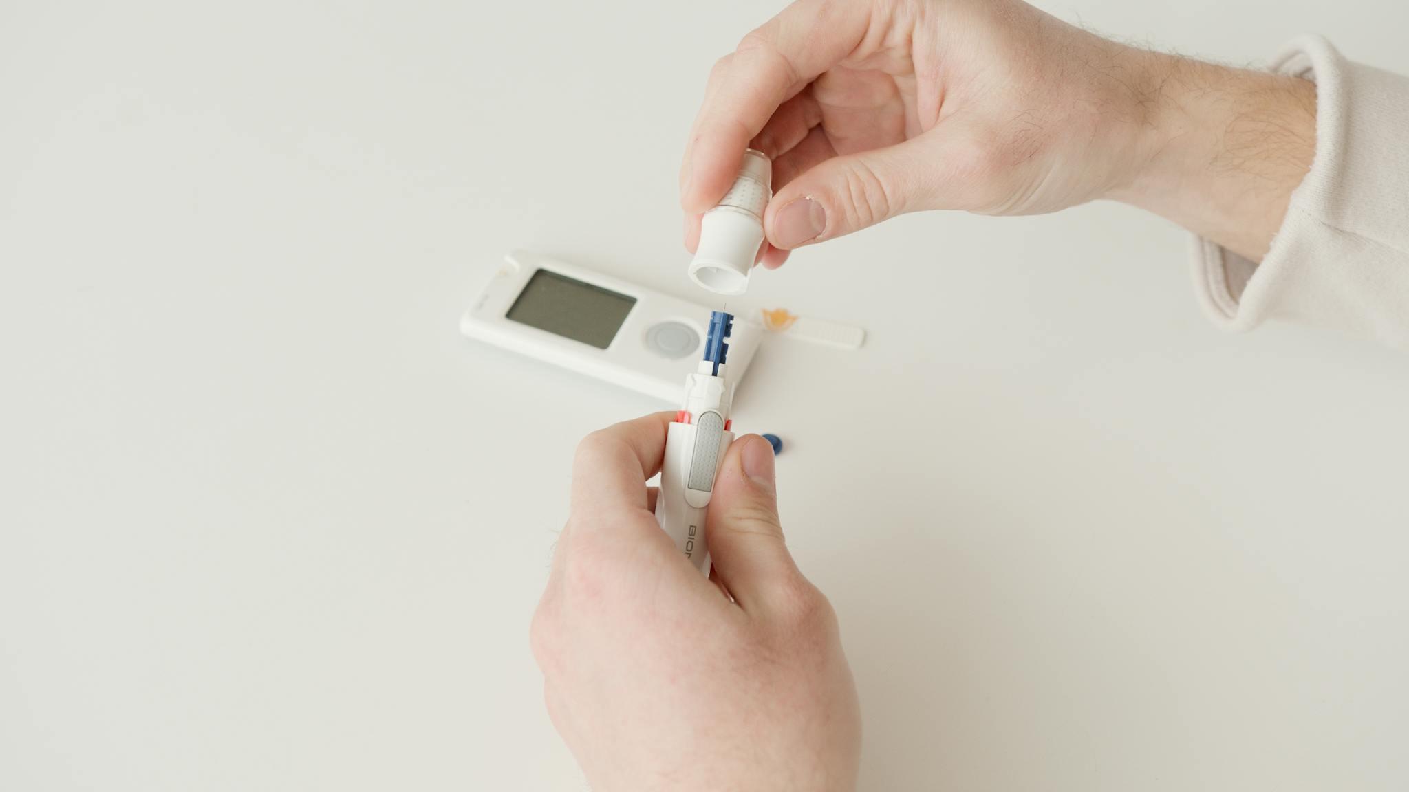 Detailed shot of hands handling a glucometer and lancet on a white background for diabetes monitoring.
